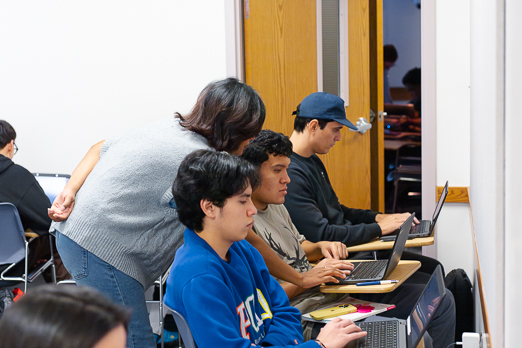 a female teacher helping a male student with two others on the side
